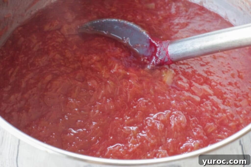 Stewed rhubarb in a saucepan after the dry strawberry gelatin has been fully mixed in, showcasing its rich color and smooth texture.
