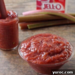 Vibrant stewed rhubarb in a glass bowl, with a jar of the compote, fresh rhubarb stalks, and a box of strawberry Jell-O in the background.