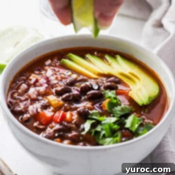 Canned Black Bean Soup in a white bowl, with a lime being squeezed over it from above, adding a fresh garnish.