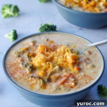 Creamy Broccoli Cheese Soup in a blue bowl with a spoon, surrounded by scattered fresh broccoli florets.