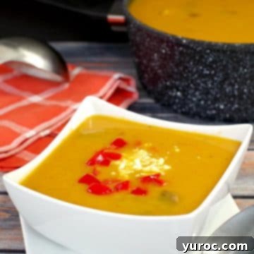 Pumpkin soup in a white bowl, garnished with a swirl of cream or coconut milk and fresh herbs, sitting on a dark wooden surface.