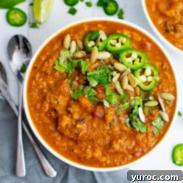 Spicy Sweet Potato Soup in a white bowl, garnished with fresh herbs, on a white surface with grey linens.