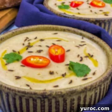 Creamy parsnip soup served in a rustic pottery bowl with a blue linen napkin on a wooden table.