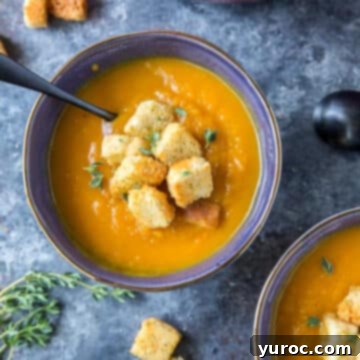 Two blue bowls filled with roasted butternut squash soup, garnished with crunchy croutons and fresh herbs.