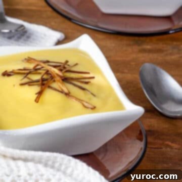 Leek and potato soup served in a white square bowl with a spoon on the side, and another bowl slightly out of focus in the background, all on a warm brown wooden surface.