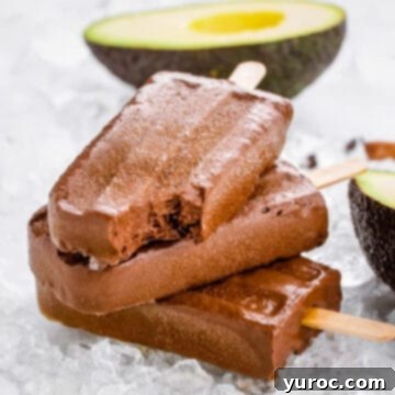 Three healthy fudgesicles piled together, with a bite taken out of the top one, and a fresh avocado in the background.