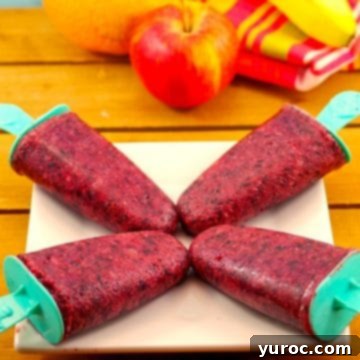 Four vibrant fruit popsicles arranged on a white plate, with a background of fresh fruit.