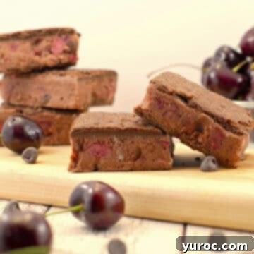 Weight Watchers Black Forest ice cream sandwiches arranged on a cutting board, with more stacked in the background and a bowl of fresh cherries.