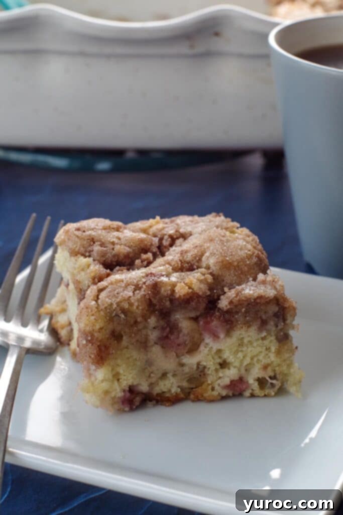 piece of rhubarb coffee cake on a white plate with a fork on the side, on a blue surface