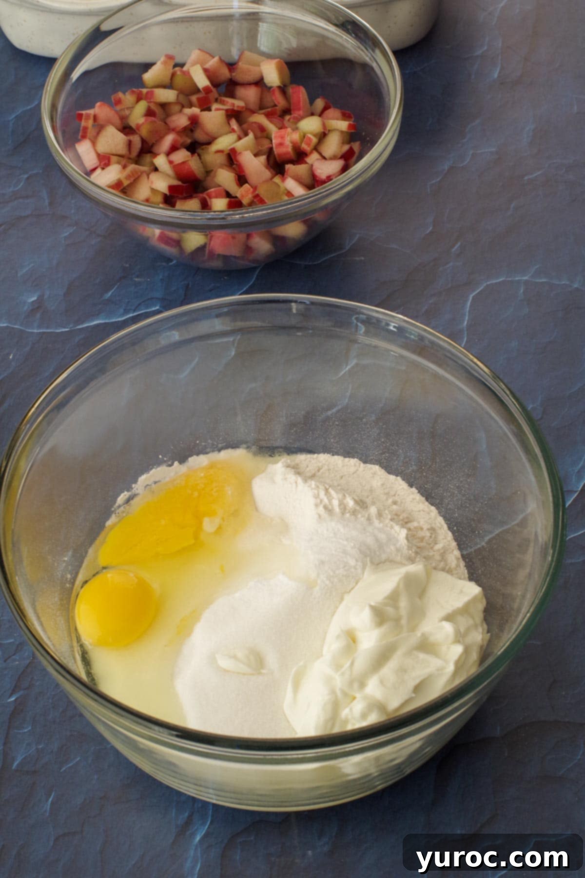 egg, flour and sugar in a large glass bowl with a glass bowl of rhubarb in background