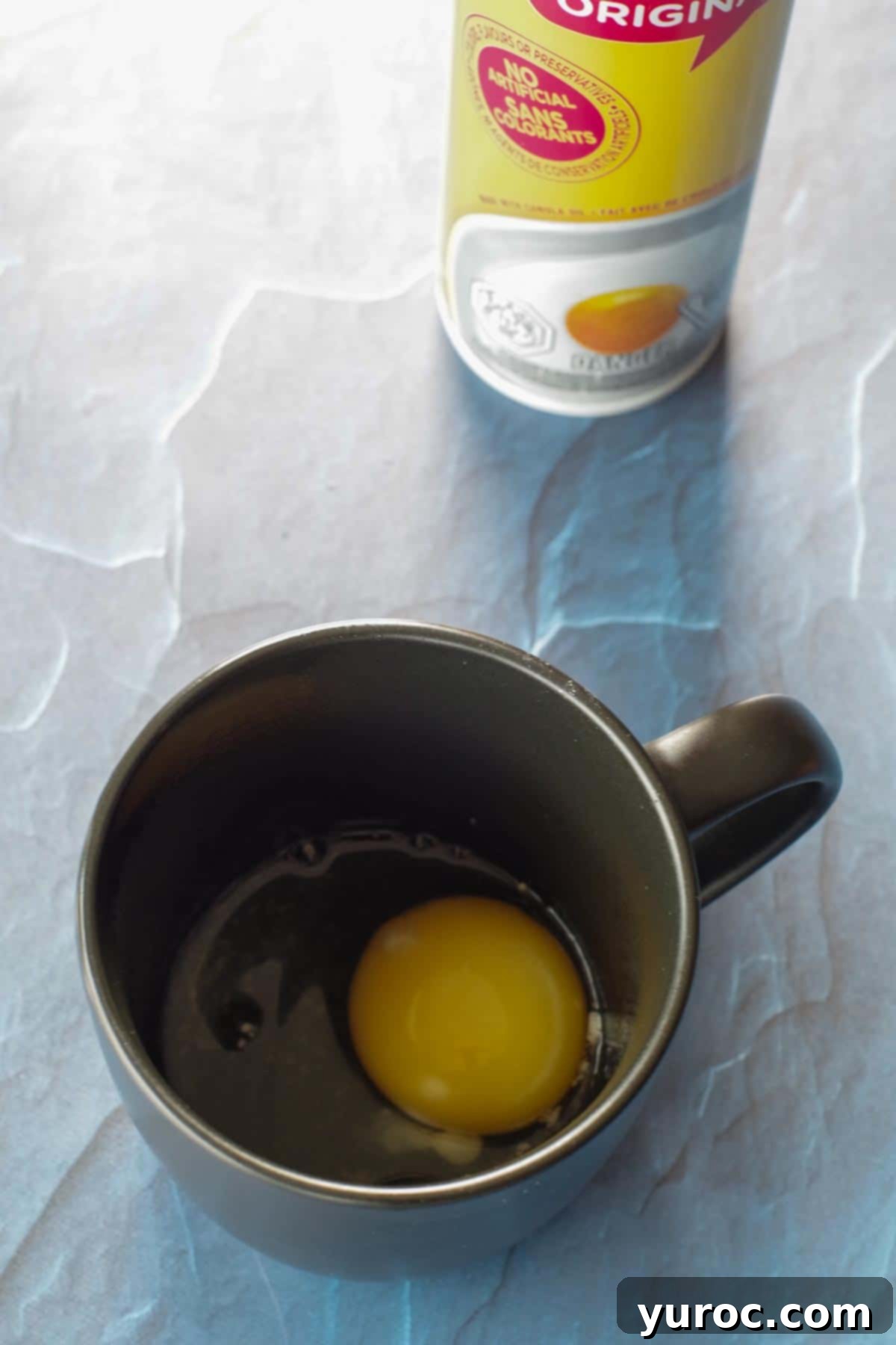 An egg in a coffee mug, demonstrating how to make a quick microwave poached egg, with a can of non-stick cooking spray in the background.