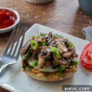 Delicious Mozza Mushroom Breakfast Sandwich on a white plate, served with a side of sliced tomato and a small dish of ketchup in the background.