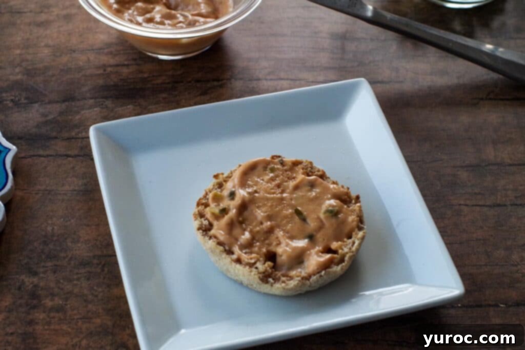 Toasted English muffin halves spread with Dijon sauce, ready for toppings.