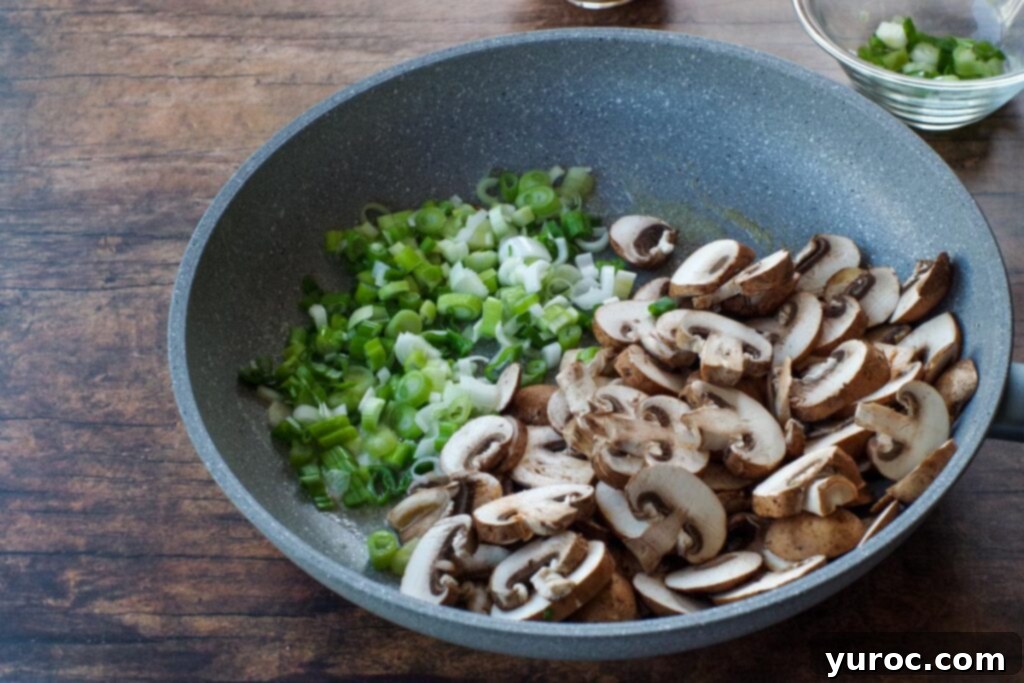 Sliced mushrooms and chopped green onions being sautéed in butter in a large skillet.