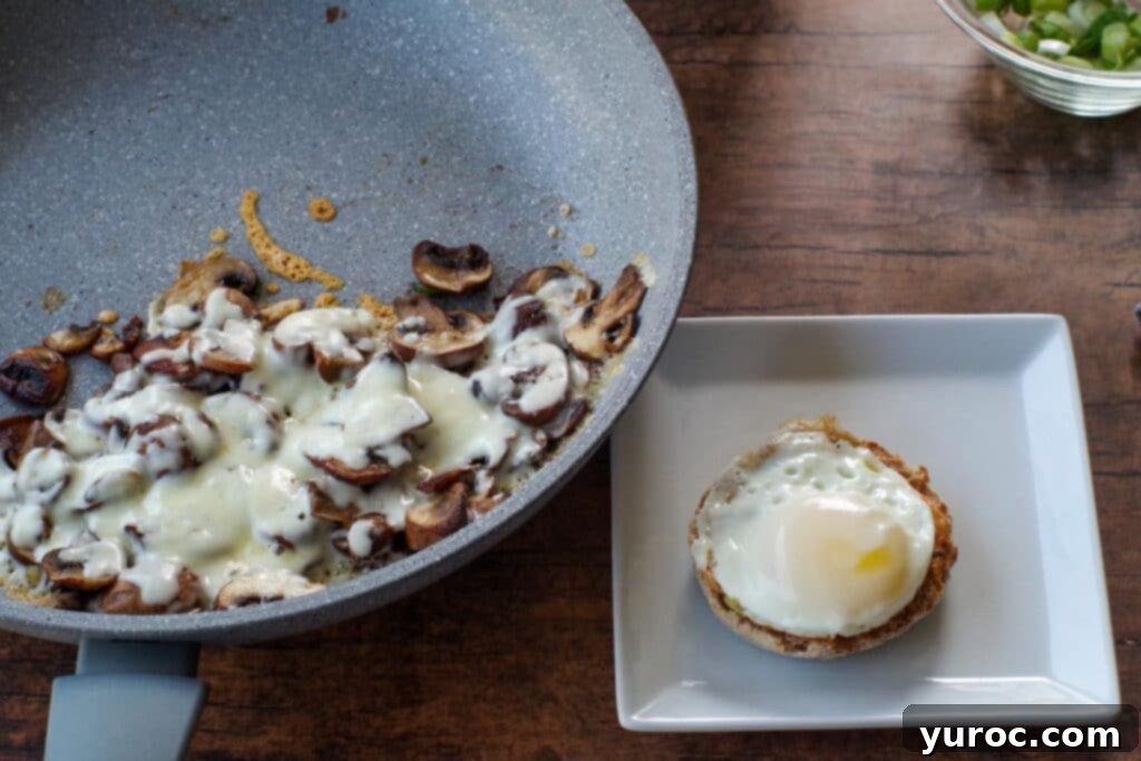 Melted mozzarella cheese over sautéed mushrooms in a skillet, alongside a cooked egg.