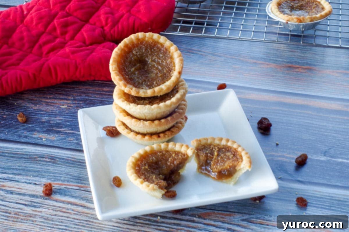 4 butter tarts stacked on a white plate, with a butter tart split in half in front of the stack