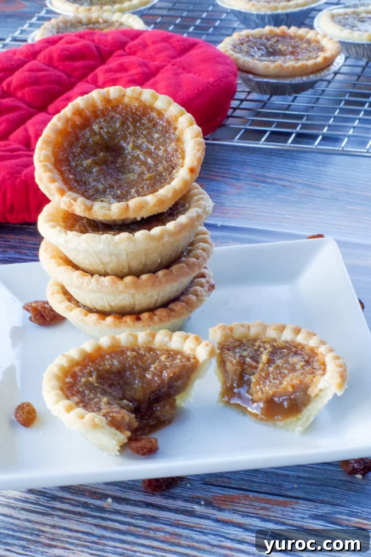 4 butter tarts stacked on a white plate, with a butter tart split in half in front of the stack