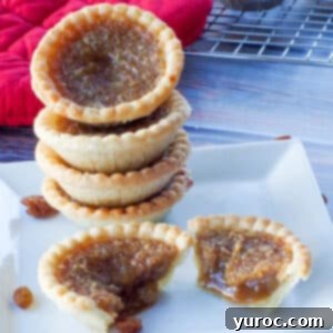 4 butter tarts stacked on a white plate, with a butter tart split in half in front of the stack