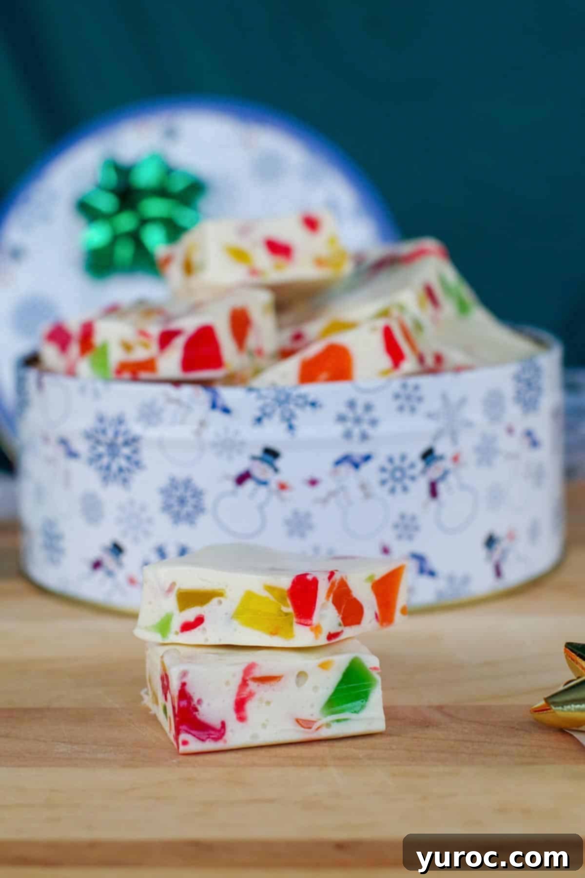 Christmas nougat candy in a Christmas tin with 2 pieces of nougat sitting on cutting board, ready for gifting