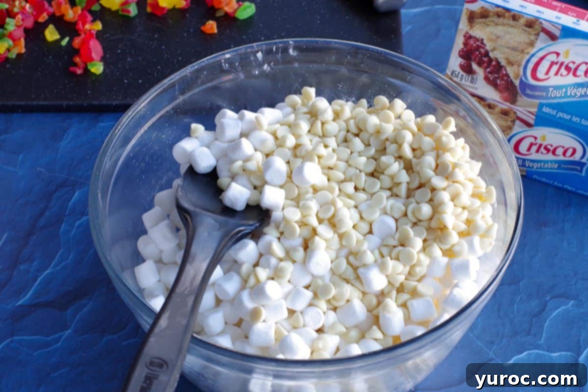 marshmallows, white chocolate chips and butter in a large glass bowl with a black spatula