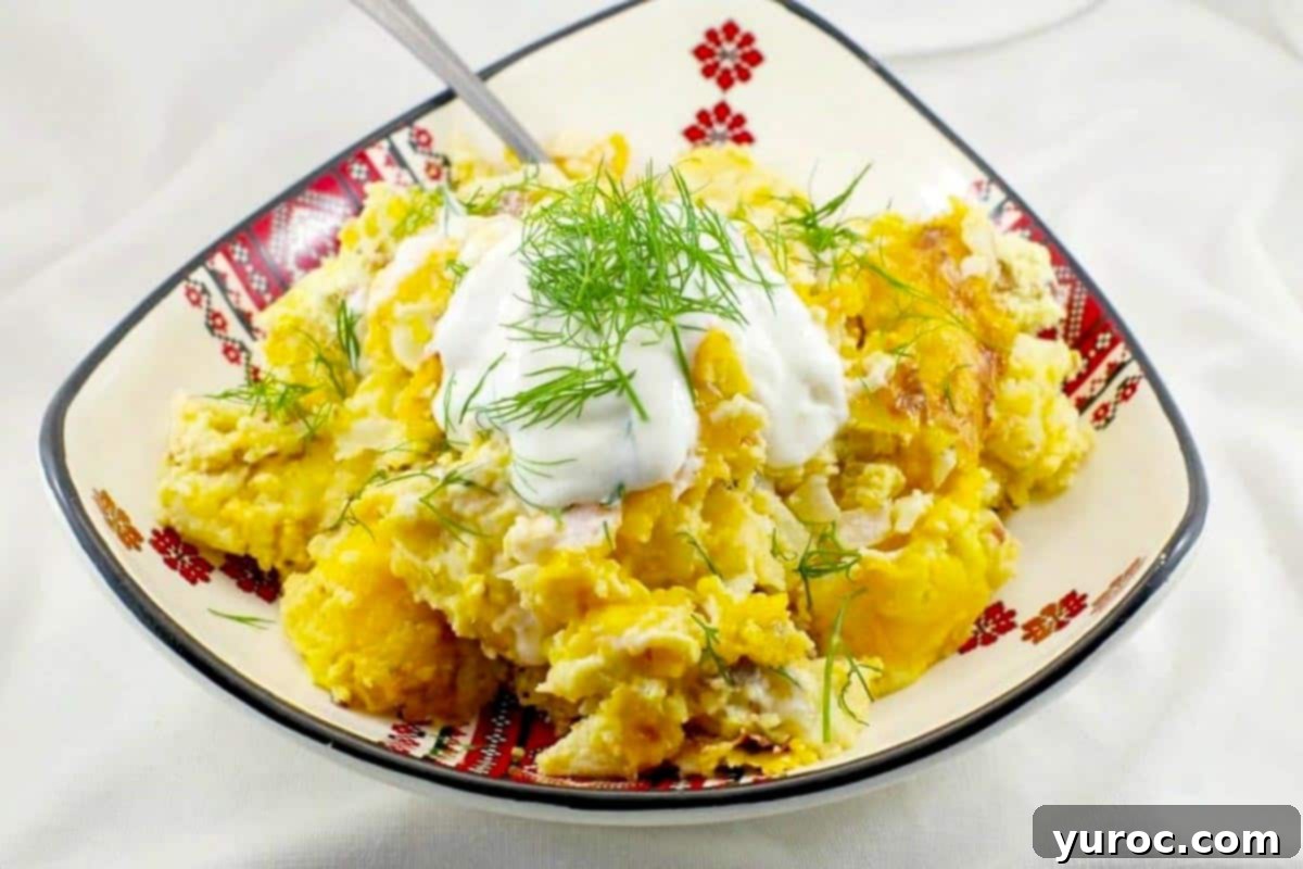 pierogi breakfast casserole in a Ukrainian print dish on light grey marble surface. A beautifully baked Pierogi Breakfast Casserole, garnished with fresh dill, served in a decorative Ukrainian bowl.