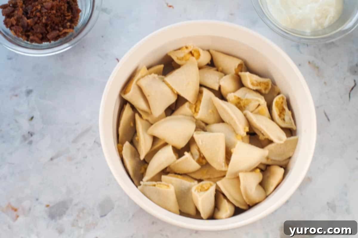 Perogies cut in half in a white casserole dish. Defrosted potato and cheese pierogies are neatly arranged at the bottom of the dish.