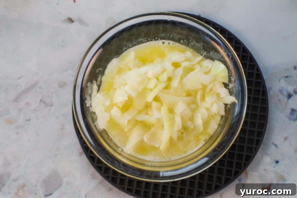 Onions chopped and cooked in butter in a small glass bowl on a black silicone trivet. Golden-brown caramelized onions ready to be added to the casserole.