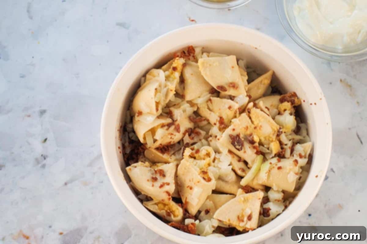 Perogies in casserole dish with cooked onions and butter and bacon bits poured over them. The pierogies are covered with a delicious layer of golden onions and crispy bacon.