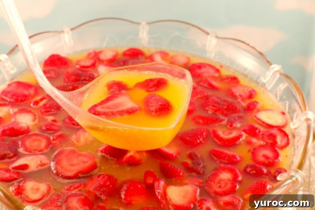 Effortless Rhubarb Lemonade 8 A large glass punch bowl filled with a vibrant red Sparkling Strawberry Party Punch, garnished with fresh strawberries and lime slices, with glasses ready to serve.
