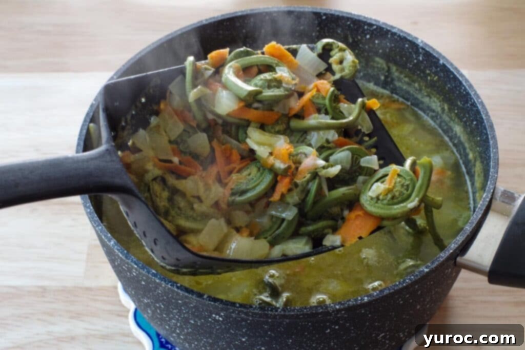 Cooked vegetables being carefully removed from the soup pot with a slotted spoon.