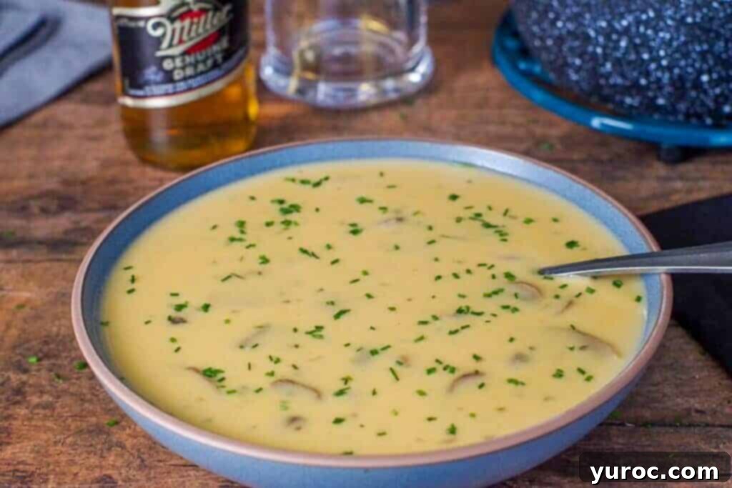 Effortless Beer Cheese Soup 1 A vibrant blue bowl filled with golden Beer Cheese Soup, a spoon resting inside. In the blurred background, a beer bottle and a mug suggest the brew's role, while the overall image highlights the soup's rich, inviting texture. The image captivates with its warmth and promises a comforting culinary experience.