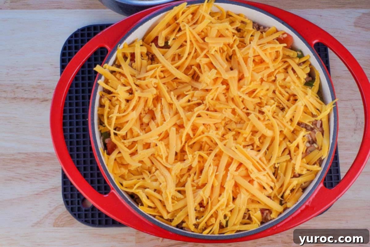 Stuffed Green Pepper Casserole covered in shredded cheese, in an orange Dutch oven.