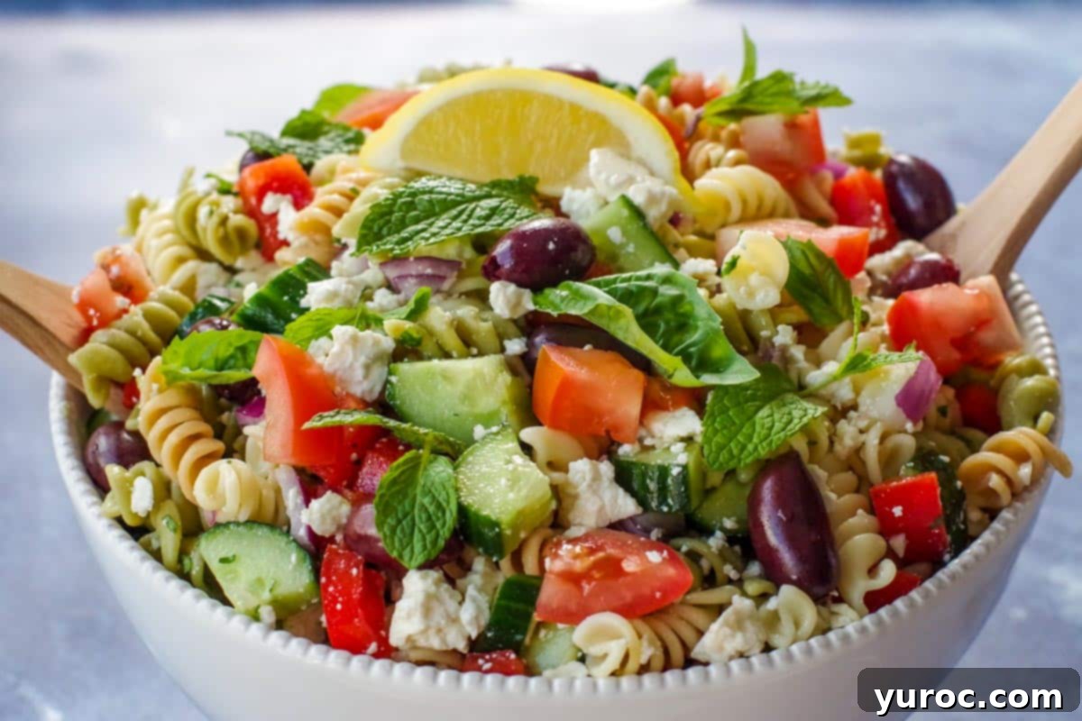 Close up photo of Greek pasta salad in a white bowl with a wooden fork and spoon (salad server).