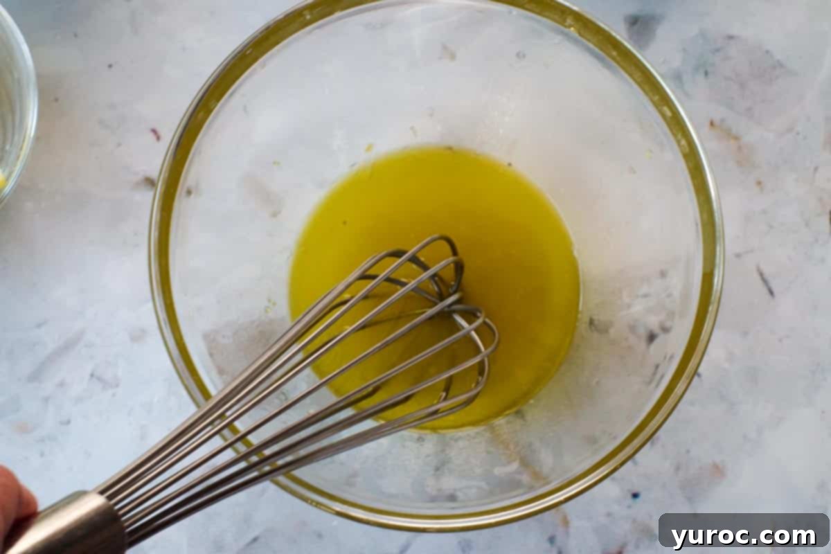 Oil, lemon juice and garlic whisked together in glass bowl with metal whisk.