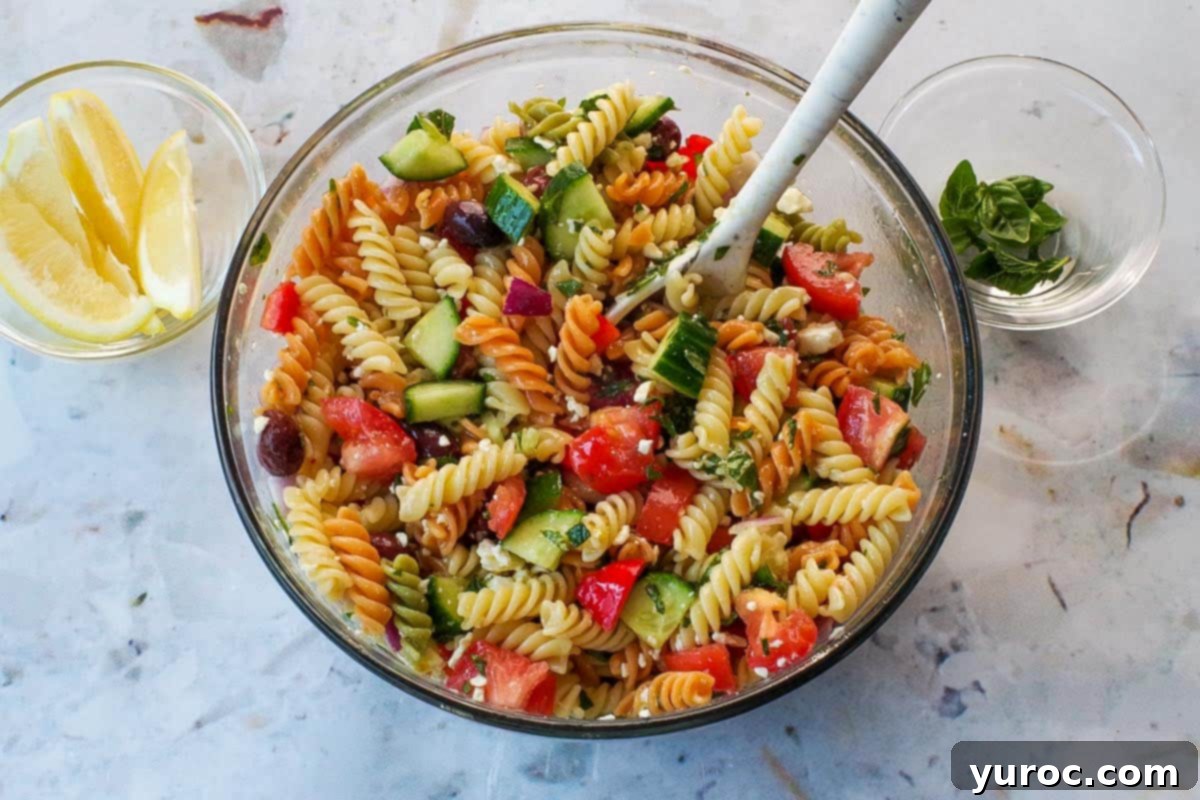 Salad dressing added to pasta and other ingredients in large glass bowl with spoon.