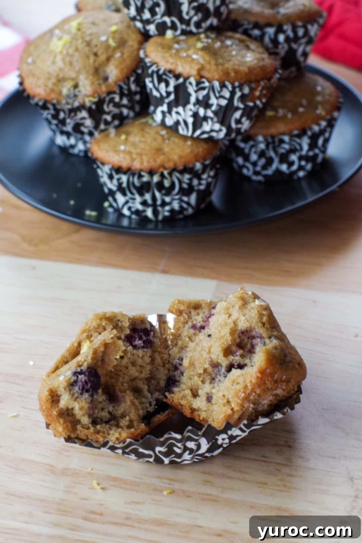 Heavenly Saskatoon Berry Muffins 11 Saskatoon berry muffin split in half on a muffin liner and a plate of more muffins in the background