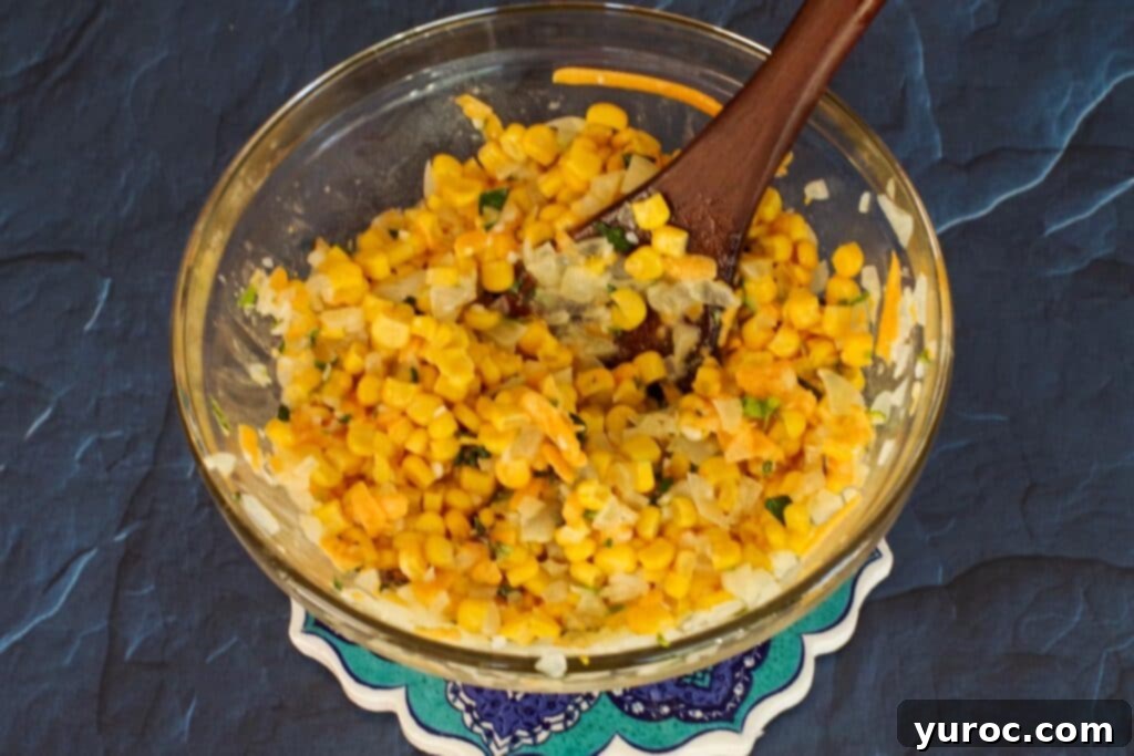 corn, herbs, and cheese mixed into onion mixture in glass bowl