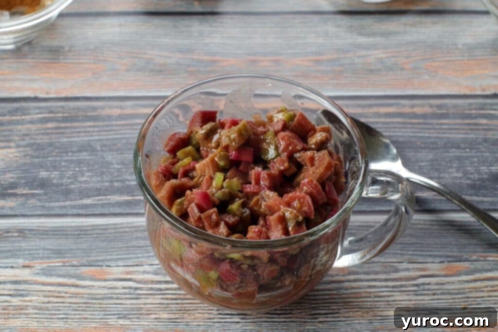 The prepared rhubarb filling mixture carefully scooped into a microwave-safe glass mug, forming the base layer for the crisp and ready for the topping.