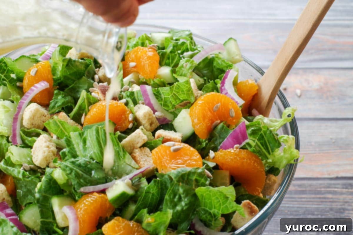 Mandarin orange salad in a large glass bowl with dressing being poured on it from a glass container