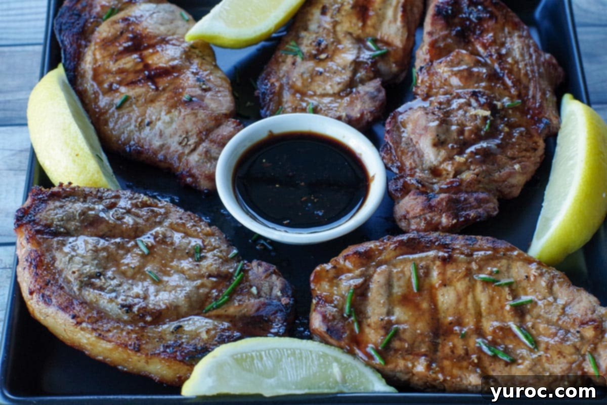 Five pieces of marinated pork on a black platter with lemon wedges and a small dish of soy sauce in the middle, ready to be served with the salad.