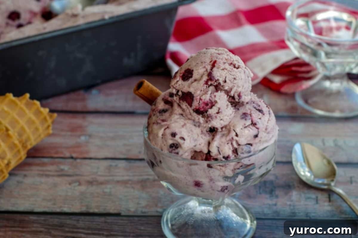 Saskatoon Berry Ice Cream in a glass dish on a wooden surface with a loaf pan of more ice cream in the background, showing the creamy texture