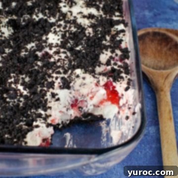 15 Easy No Bake Potluck Desserts 3 cherry cha cha dessert in glass container, with some scooped out and wooden spoon on right hand side (all on blue background)