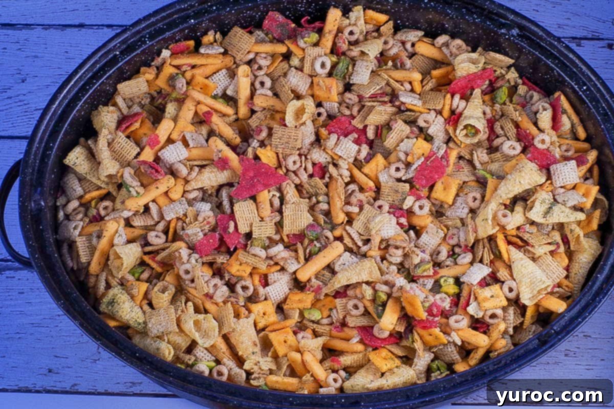 The seasoned snack mix is poured into a large roasting pan, spread out evenly for baking.