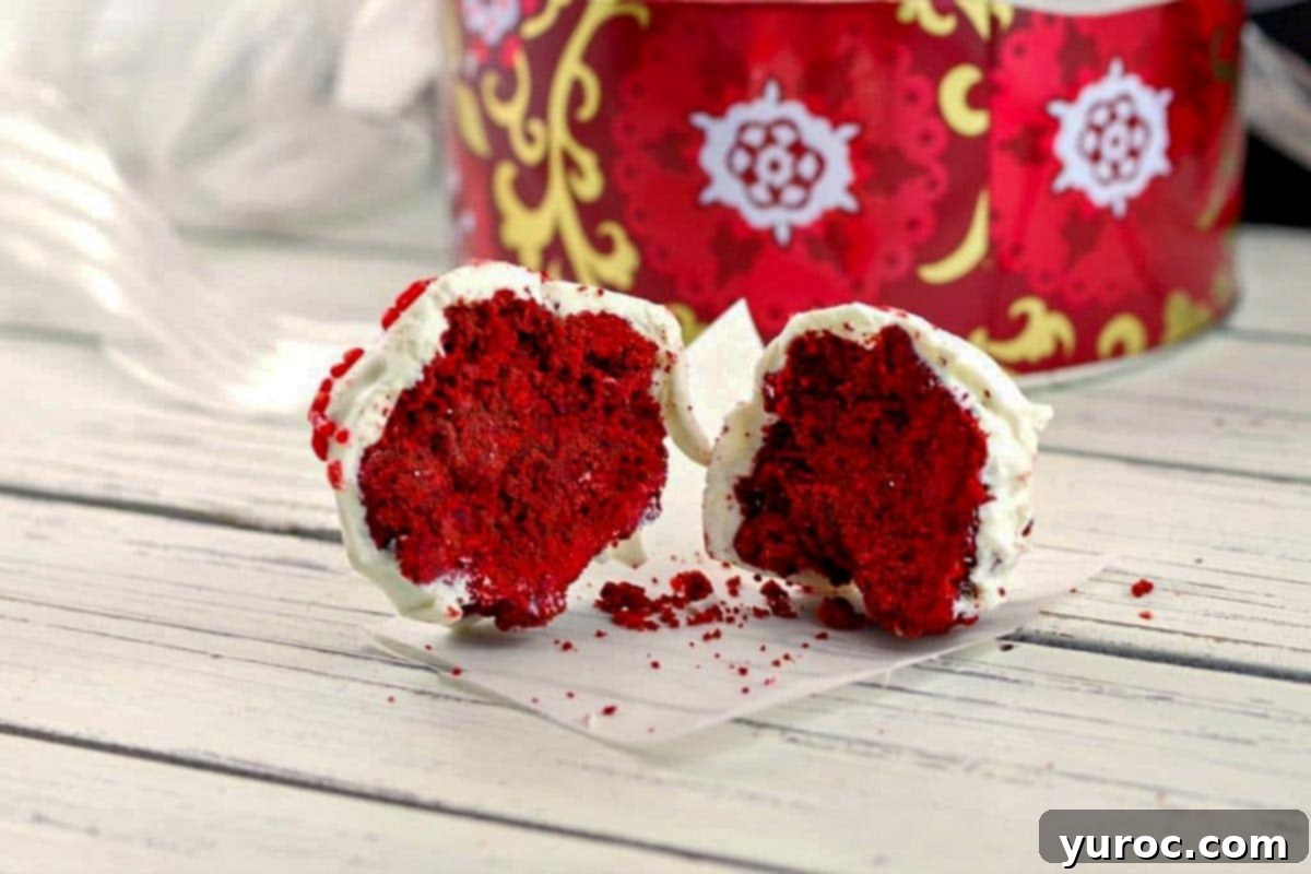 Red velvet brownie bite split in half, on a white wooden surface with Christmas cookie tin in background