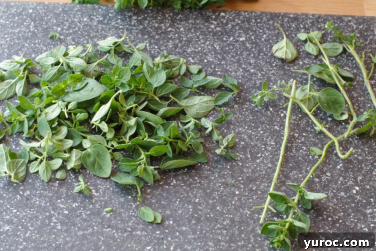 oregano leaves being removed from stems on grey cutting board