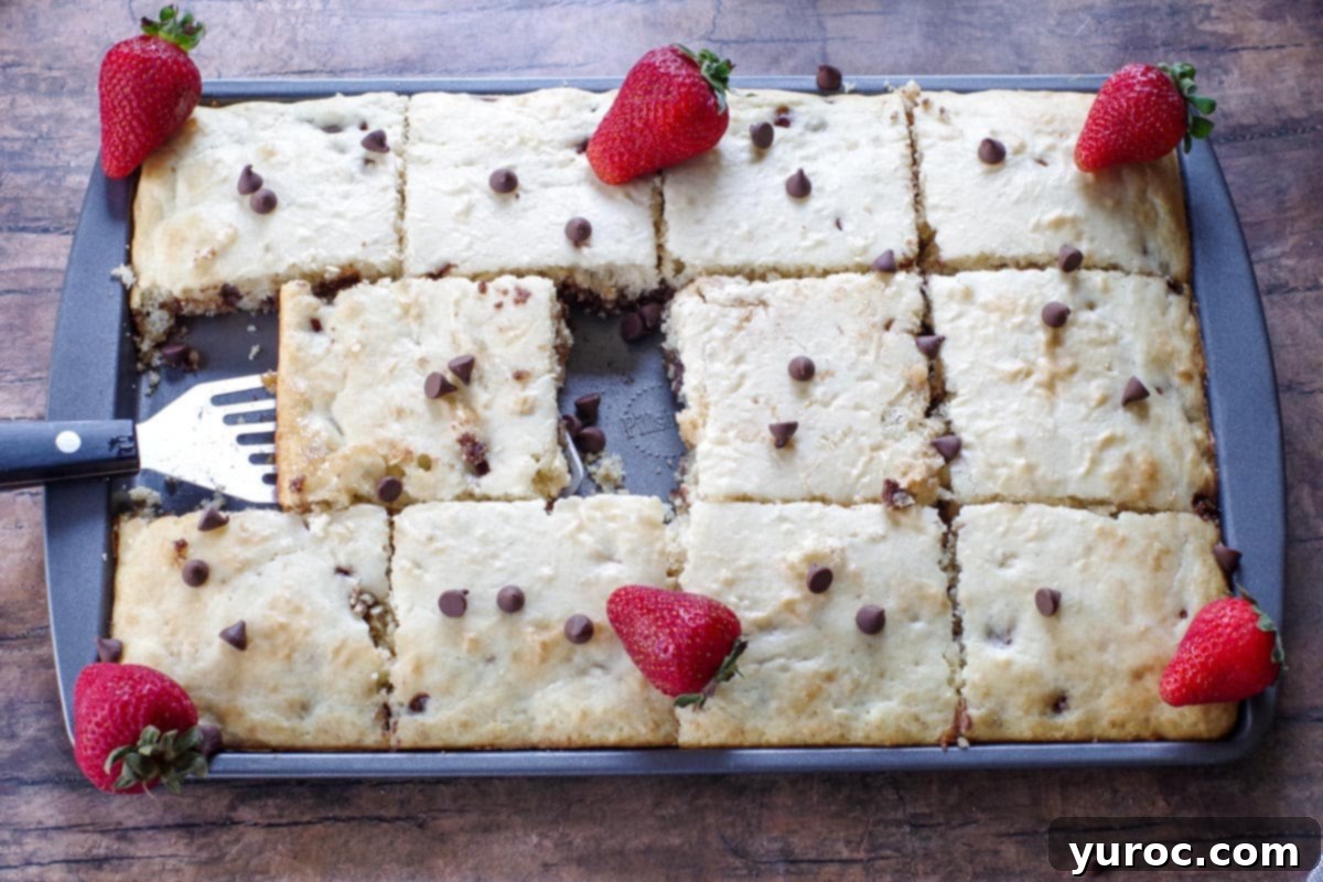 Effortless Sheet Pan Chocolate Chip Pancakes 13 sheet pan chocolate chip pancakes with strawberries on top, with one missing and a spatula removing one pancakes