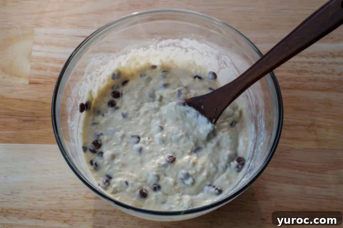 Effortless Sheet Pan Chocolate Chip Pancakes 7 milk chocolate chips added to mixture in glass bowl with wooden spoon