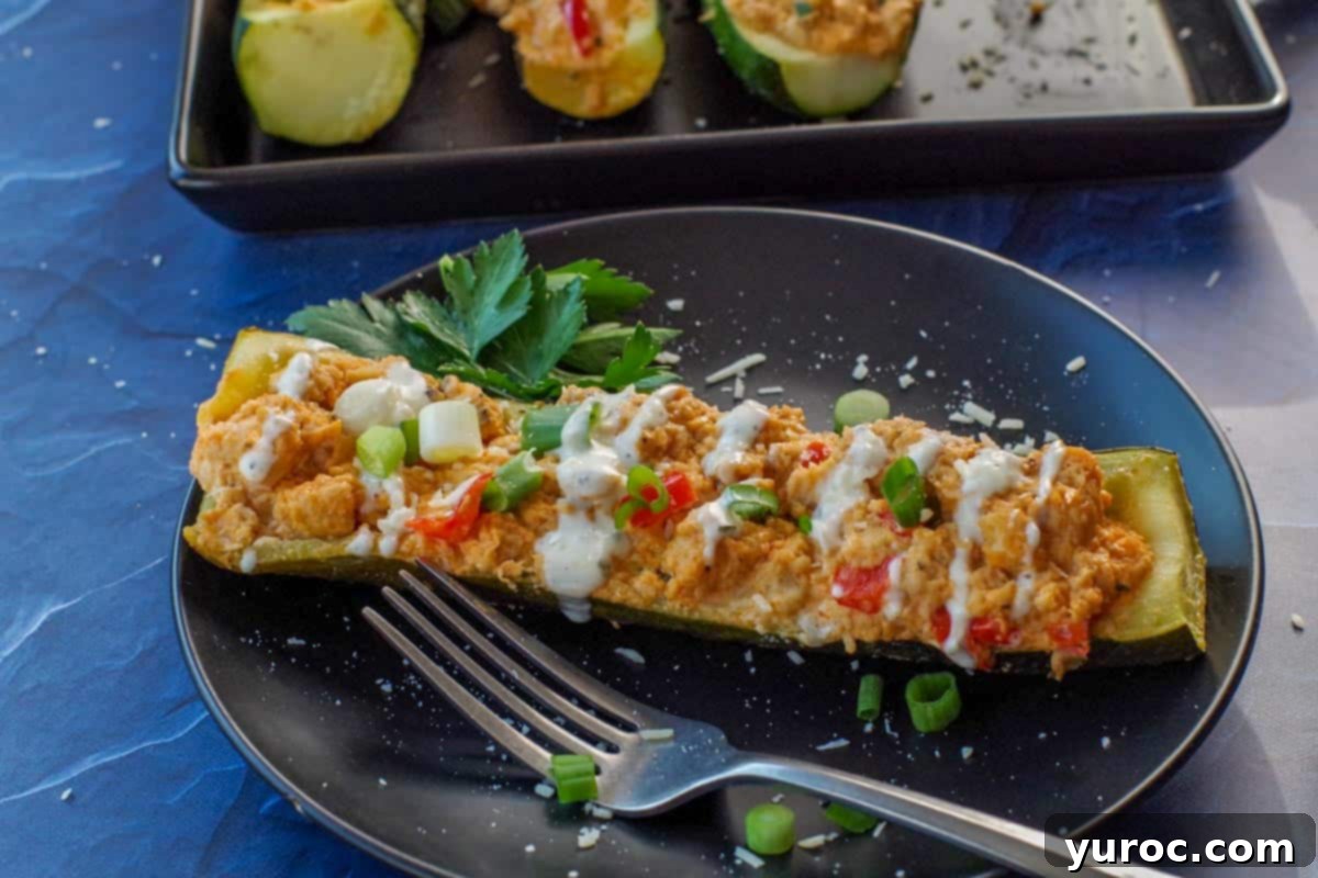 zucchini boat on black plate with black tray of zucchini boats in the background