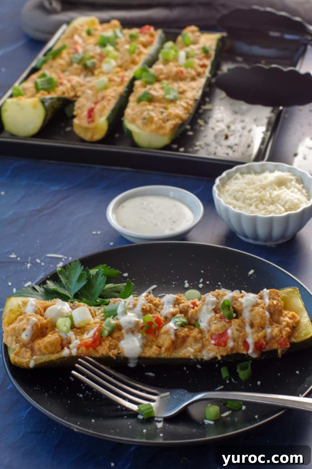 buffalo chicken zucchini boat on black plate with tray of zucchini boats in the background