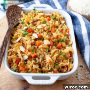 vegetarian rice pilaf in a white casserole dish on wooden surface, with large spoon in it